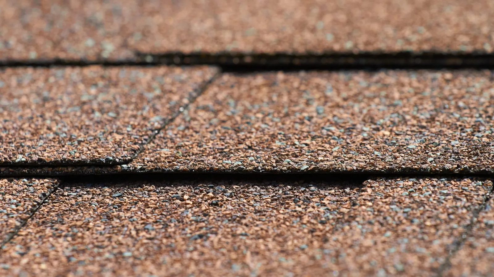 Macro of brown asphalt shingle granules and overlapping tab edges